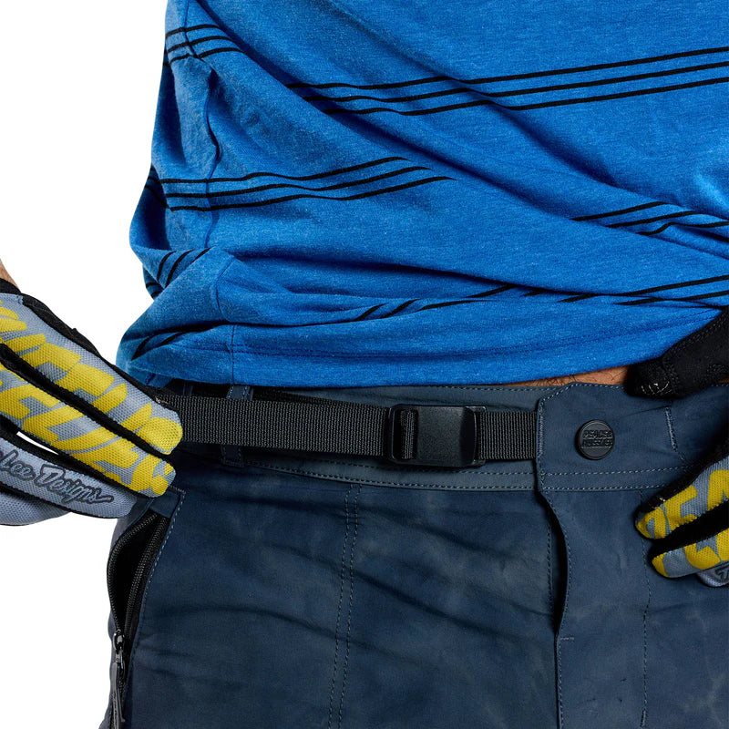 Close-up of a person wearing a blue shirt and dark pants with gloves on a white background