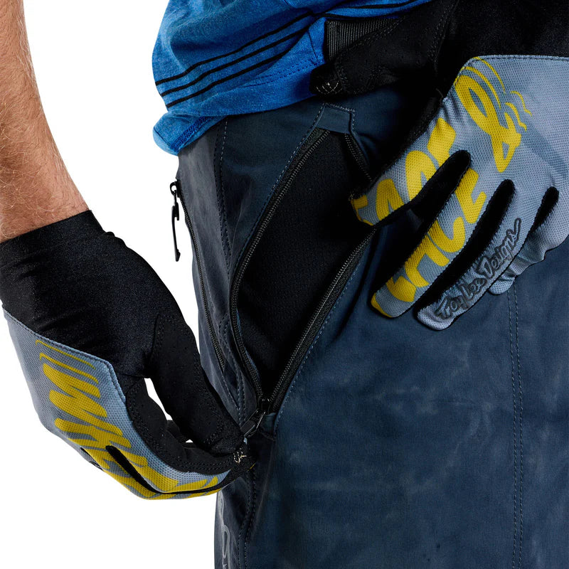 Person wearing blue pants and black gloves with yellow text, holding a blue bag.