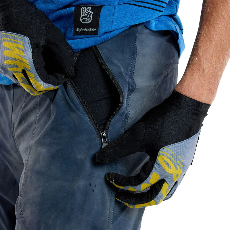 Person wearing blue pants with a pocket, black gloves with yellow accents, and a blue jacket with a visible brand logo.