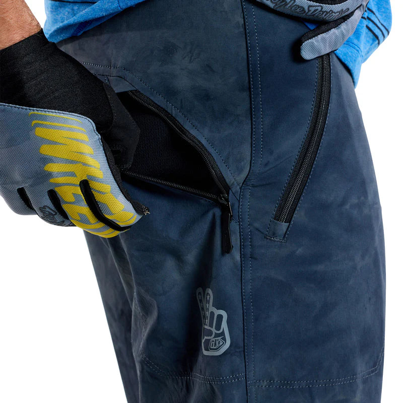 Close-up of blue pants with a brand logo, worn by a person with gloves.