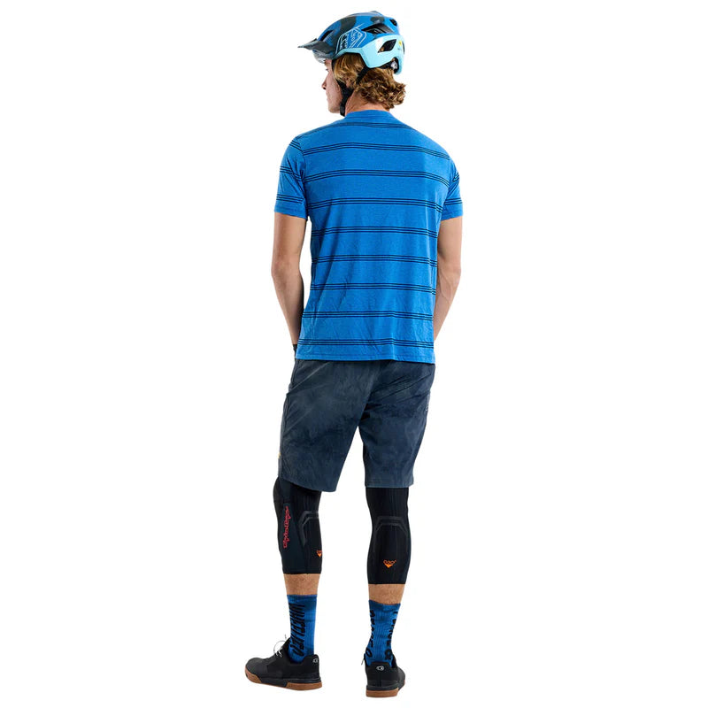 Person wearing a blue striped shirt and black shorts with knee pads on a white background