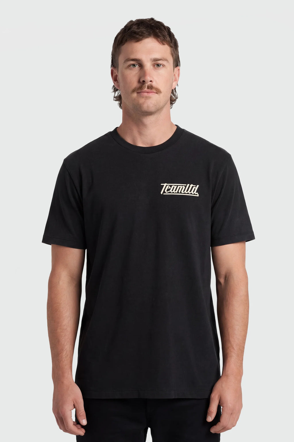 A man wearing a black short-sleeve crewneck t-shirt with a small white 'TeamTLD' logo on the left chest, photographed against a light gray studio background.