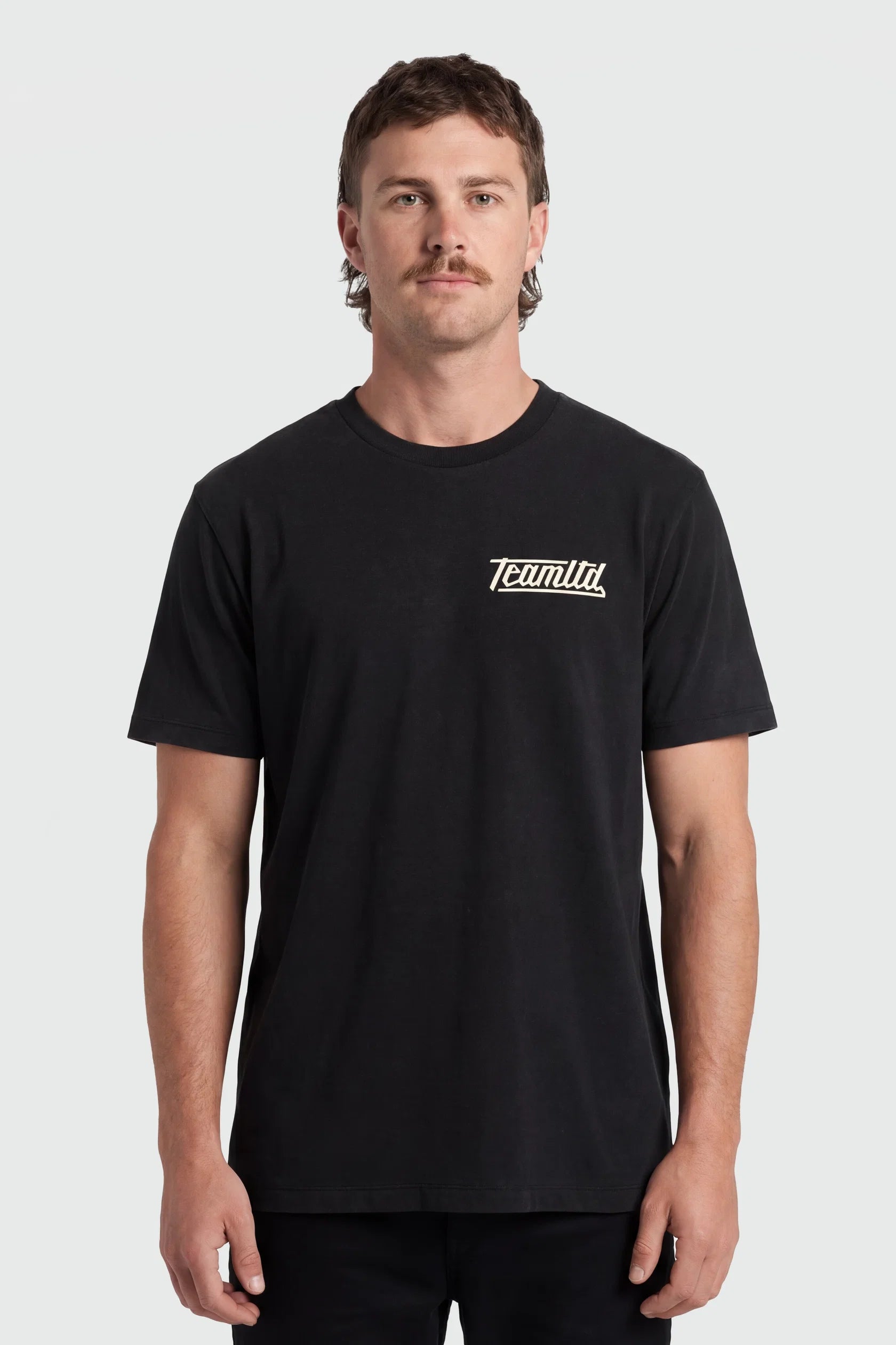 A man wearing a black short-sleeve crewneck t-shirt with a small white 'TeamTLD' logo on the left chest, photographed against a light gray studio background.