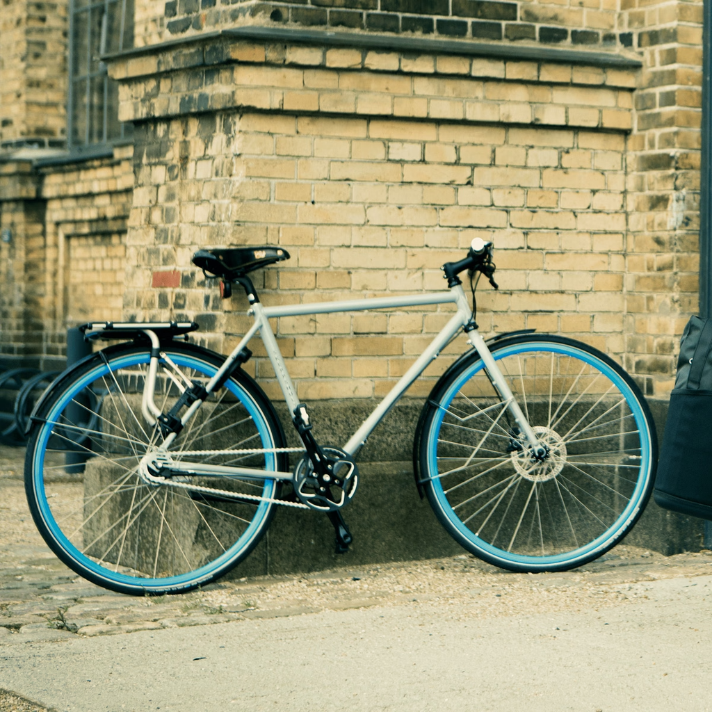 White bicycle with blue wheels leaning against a brick wall.