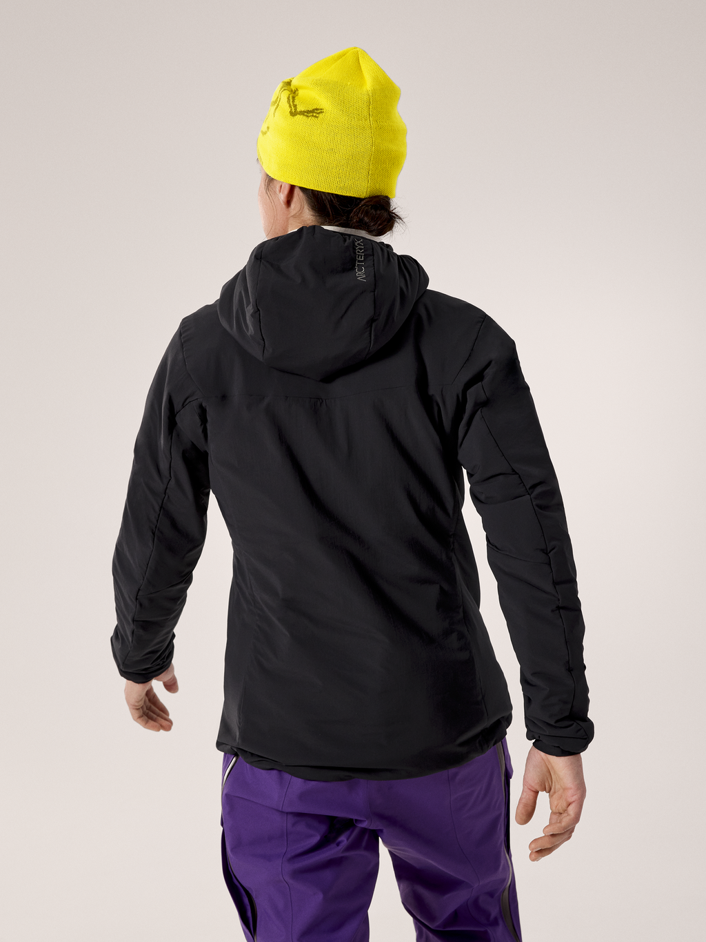 Person wearing a black jacket, yellow beanie, and purple pants on a light gray background