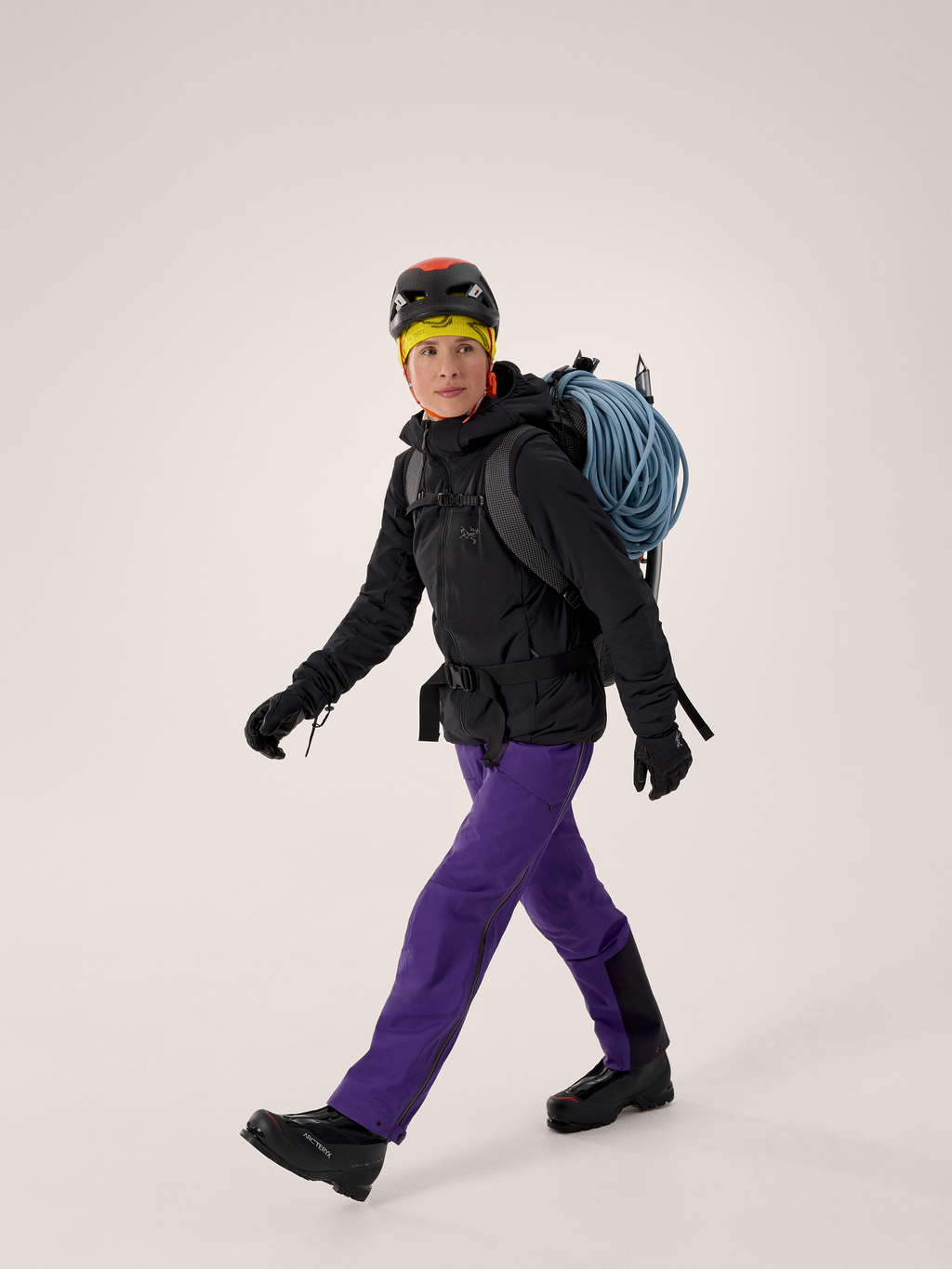 Person wearing climbing gear with a helmet, gloves, and a backpack on a plain background