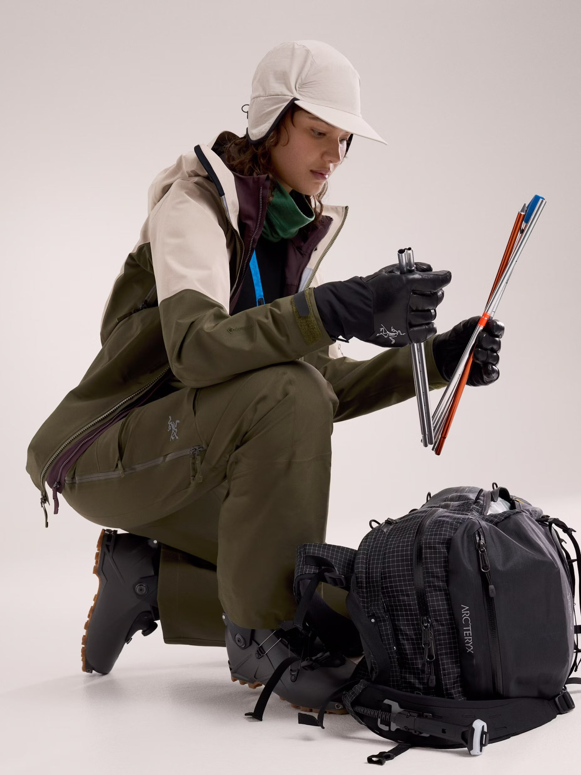 Person in outdoor gear preparing skis with a backpack on a white background