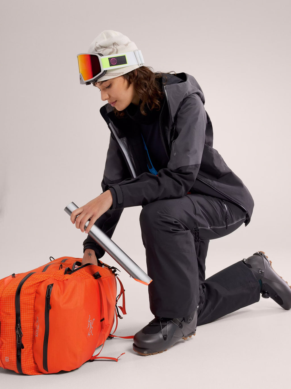Person in ski gear with an orange backpack on a light gray background