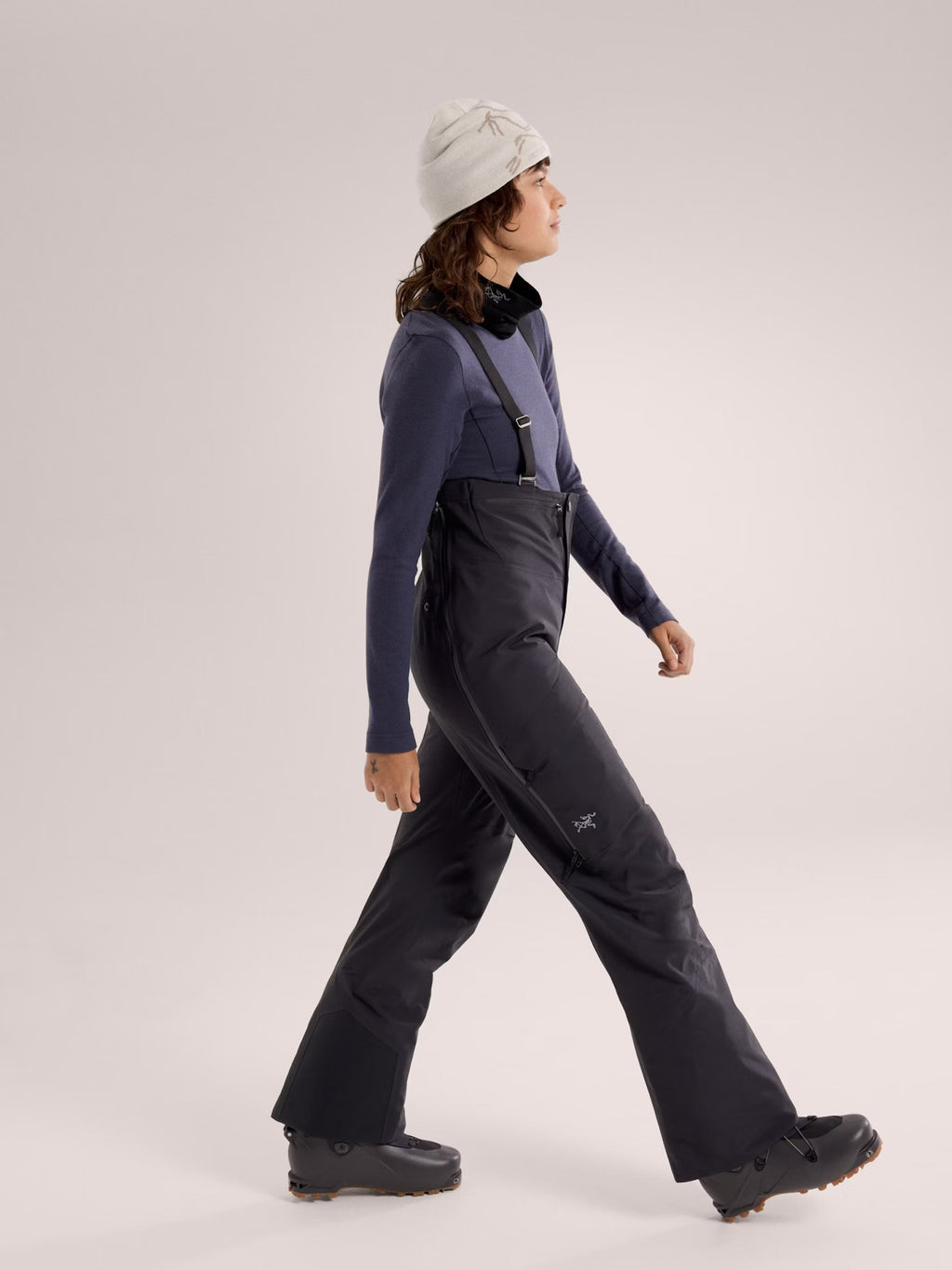 Person wearing a dark blue snowsuit with black bib and boots on a light gray background