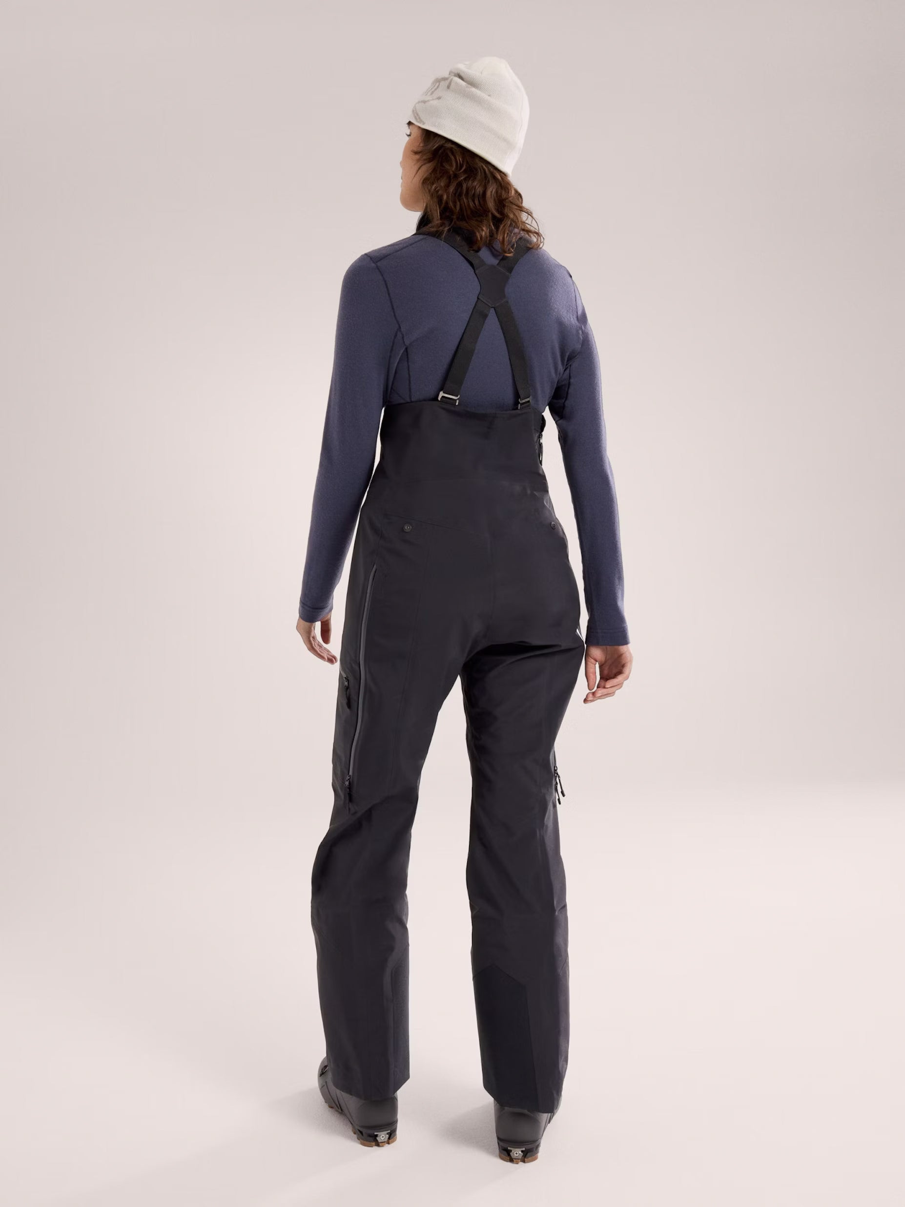 Person wearing a dark blue long-sleeve top and black bib overalls on a light gray background