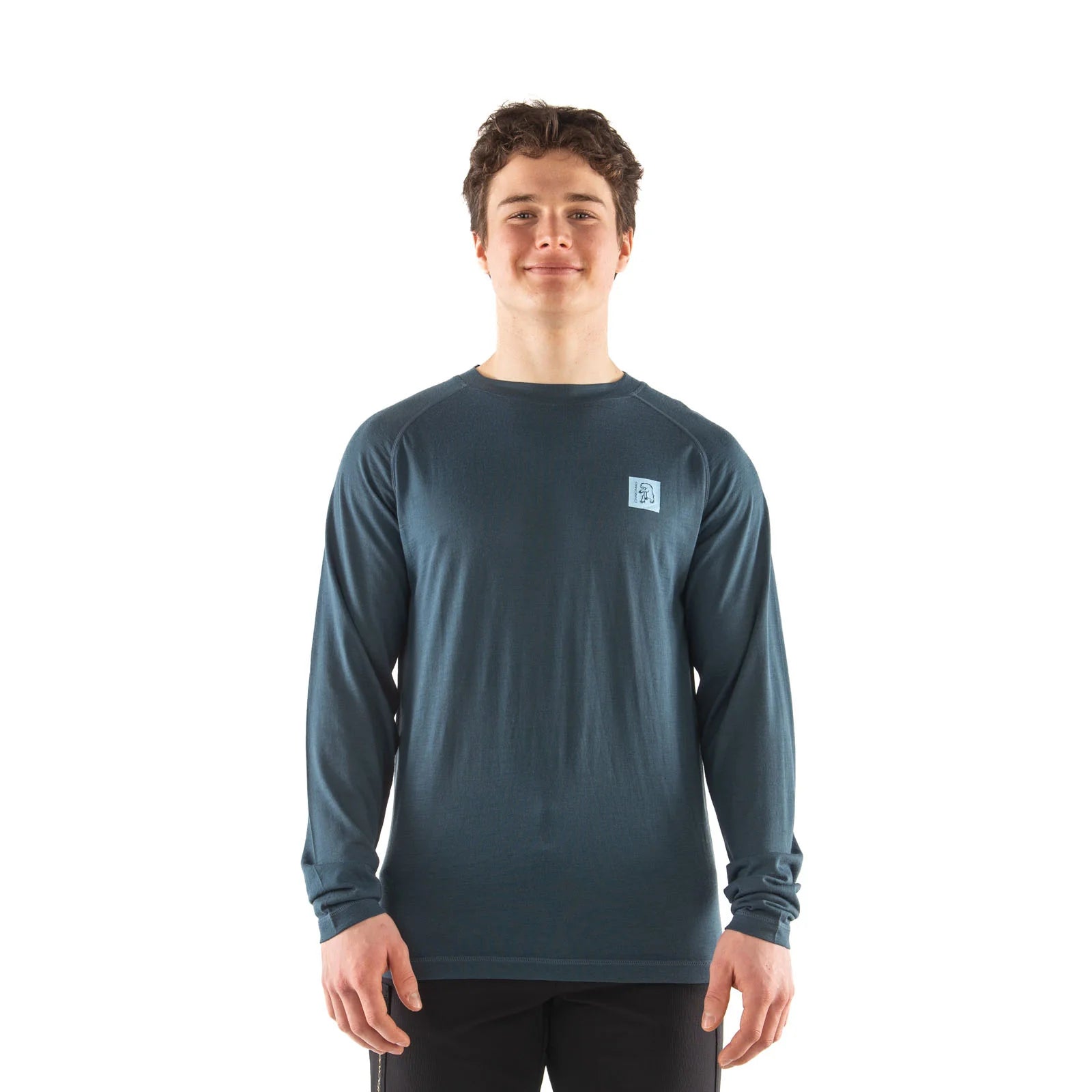 A young man wearing a dark slate blue long-sleeve performance shirt with a small square logo on the left chest, standing against a solid white background.