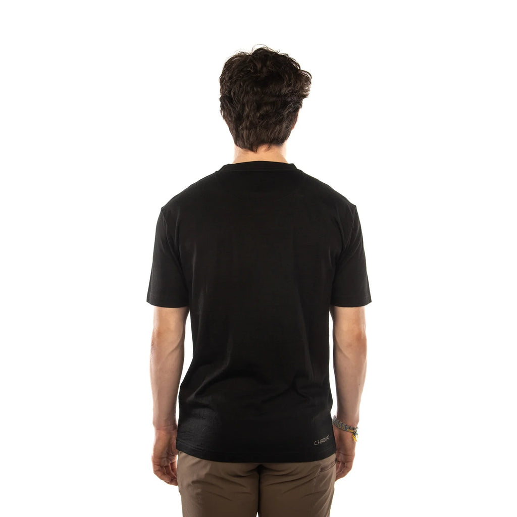 A man viewed from behind wearing a black short-sleeve crewneck t-shirt and brown pants, standing against a solid white background.
