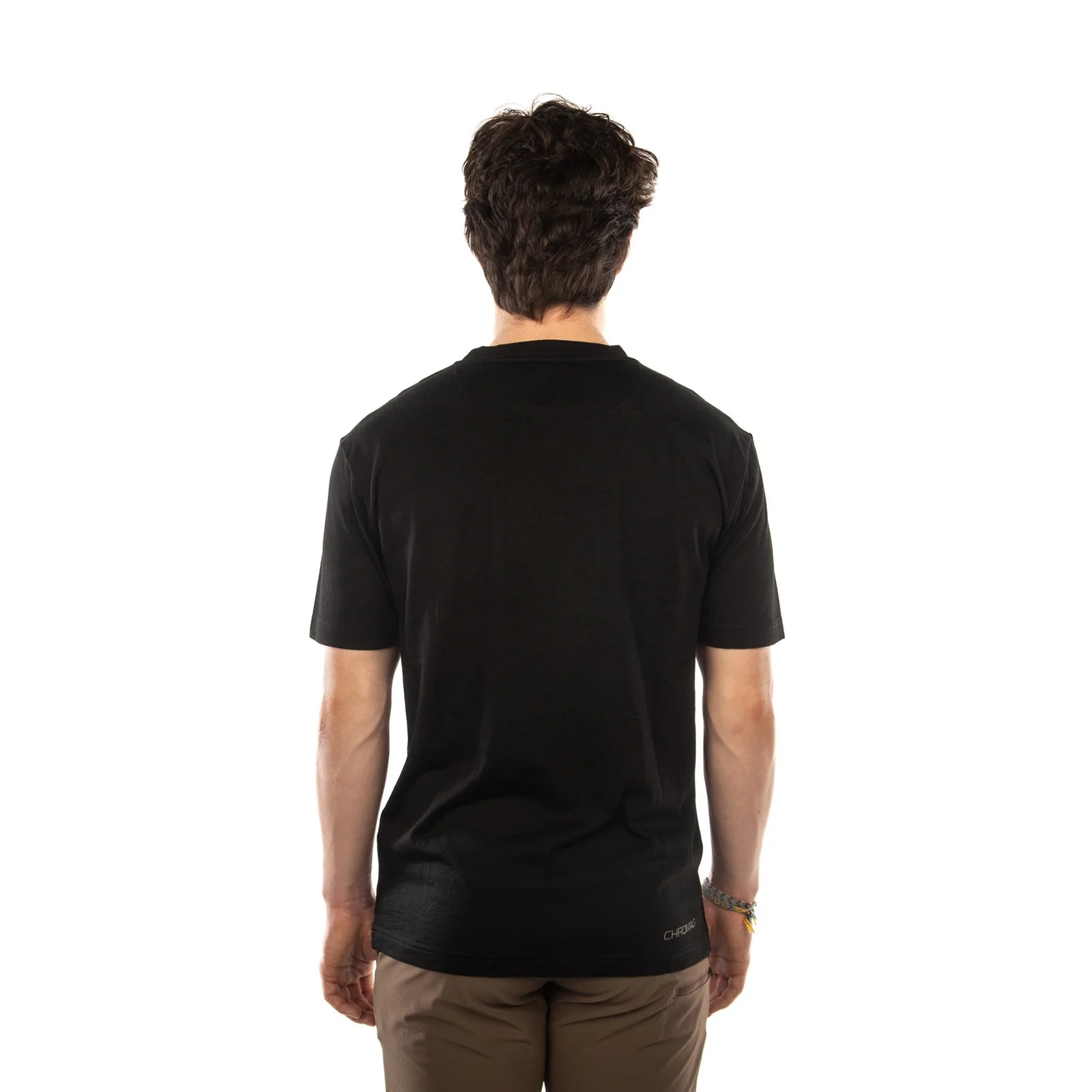 A man viewed from behind wearing a black short-sleeve crewneck t-shirt and brown pants, standing against a solid white background.