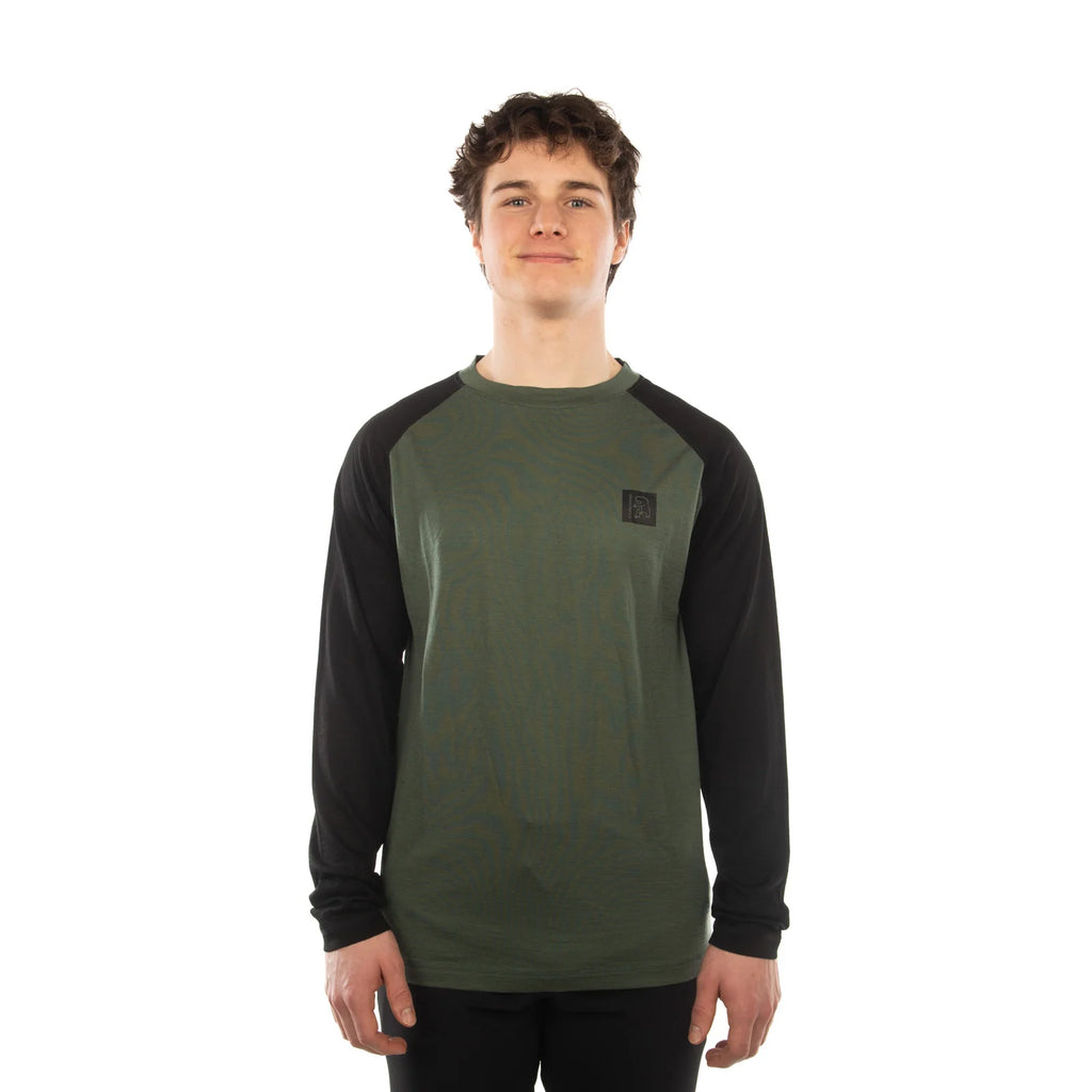 A young man wearing a long-sleeve raglan shirt with an olive green body and black sleeves, standing against a plain white background.