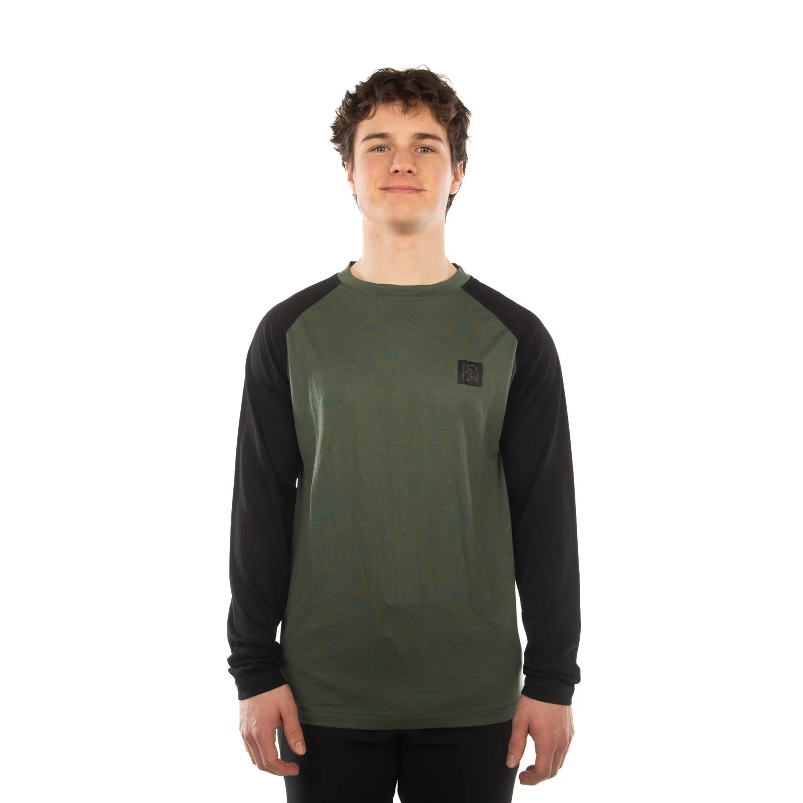 A young man wearing a long-sleeve raglan shirt with an olive green body and black sleeves, standing against a plain white background.