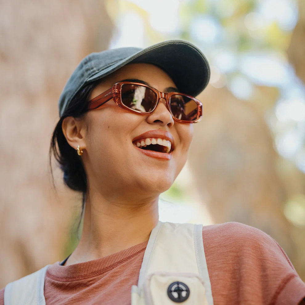 Person wearing sunglasses and a cap with a blurred natural background